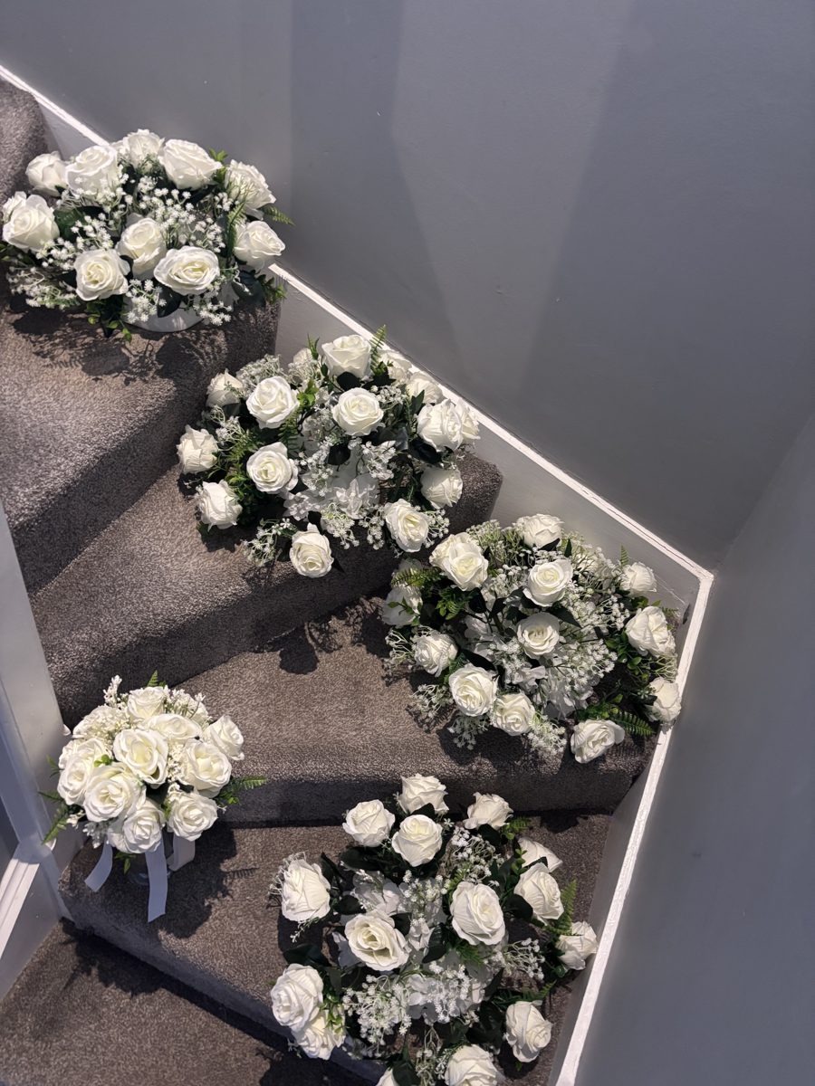 Five wedding centrepieces of cream roses and gypsophila arranged on a staircase